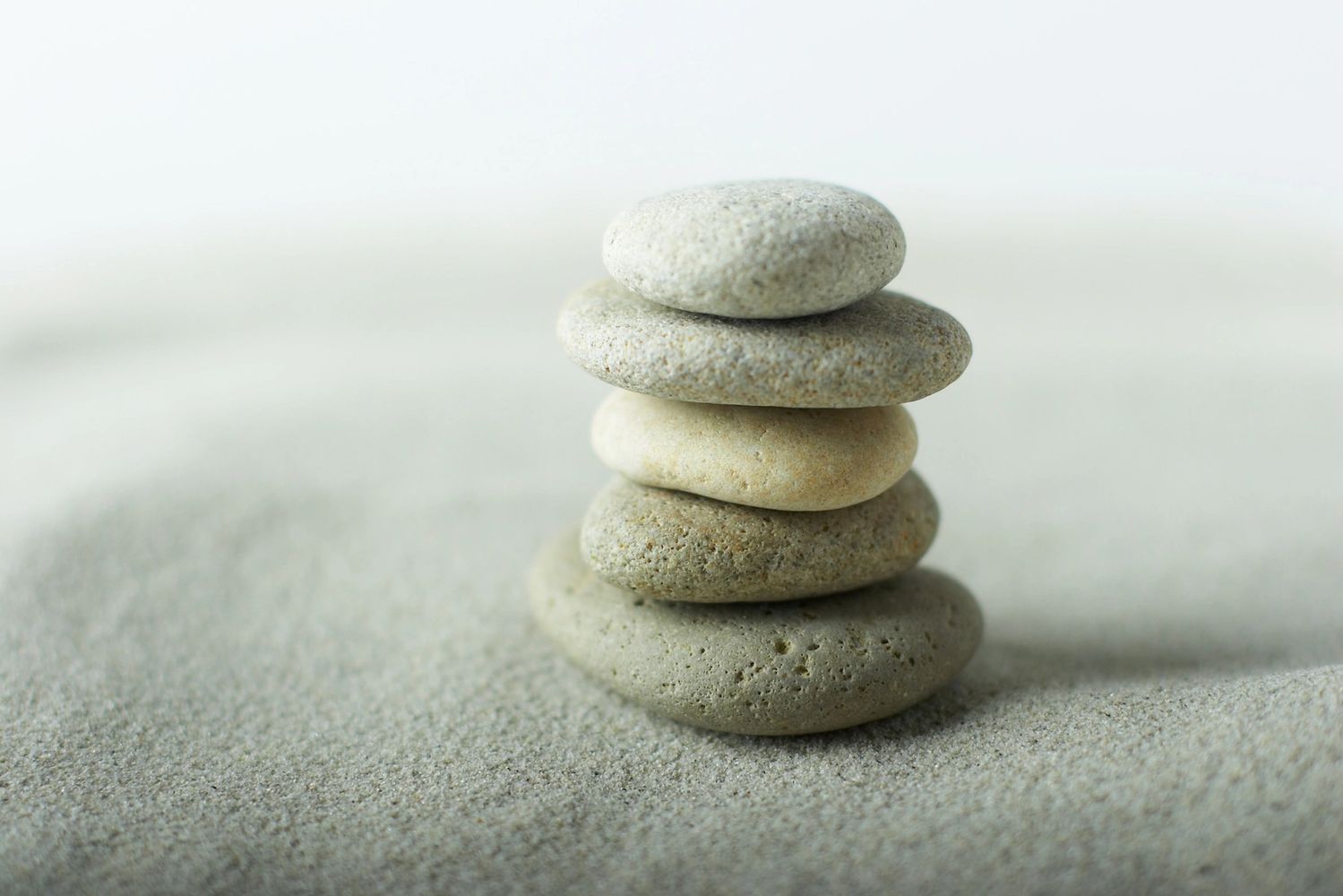 A balanced stack of smooth grey stones on sand.