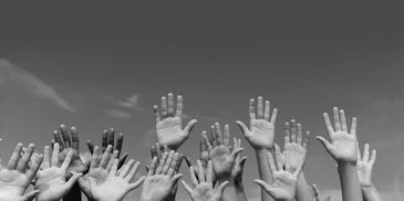A group of diverse hands raised against a clear sky.