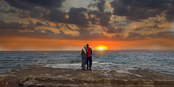 Couple embracing standing in front of a lake watching the sunset on a cloudy evening.