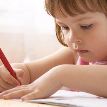 A young child focused on drawing with a red colored pencil.