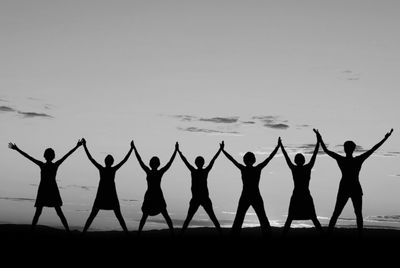 Seven people holding hands in silhouette against a sunset.