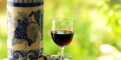 A glass of red wine with a decorative pitcher and corkscrew on a table.