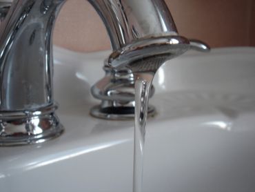 Close-up of water flowing from a shiny chrome faucet into a white sink.