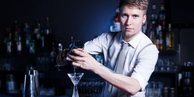 Bartender pouring a cocktail in a dimly lit bar.