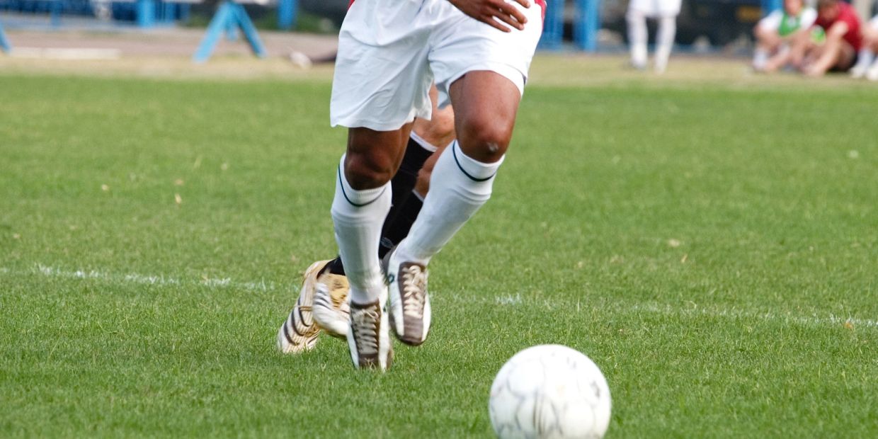 Two soccer players in motion chasing the ball on a grassy field.