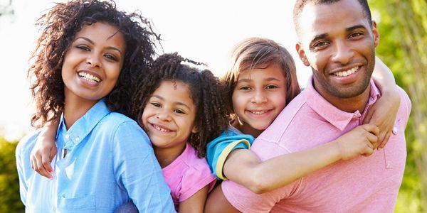 A family of four with each parent smiling and carrying a child on their backs. 