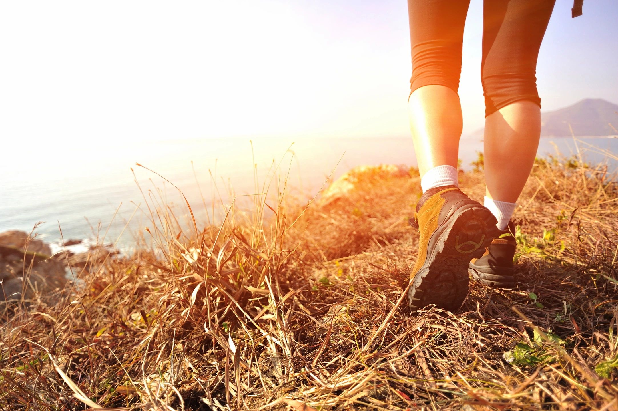 Person hiking on a sunny trail near a body of water.