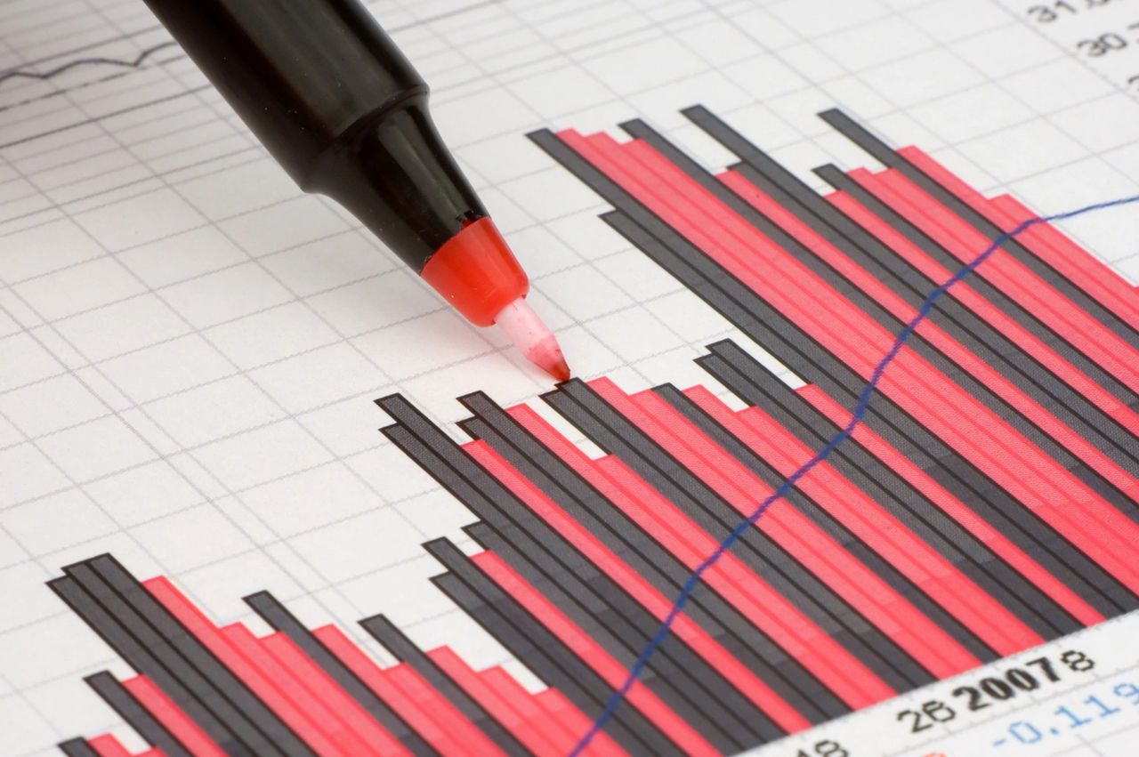 A red ink pen points to data points on a red and black line graph.