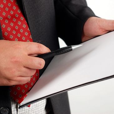 Person in suit holding pen and clipboard with blank paper.