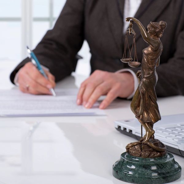 A lawyer signs a document with a Lady Justice statue in the foreground.