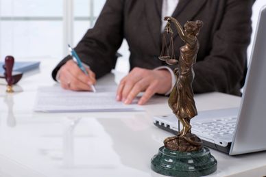 Lady Justice statue on a desk with a person writing in the background.