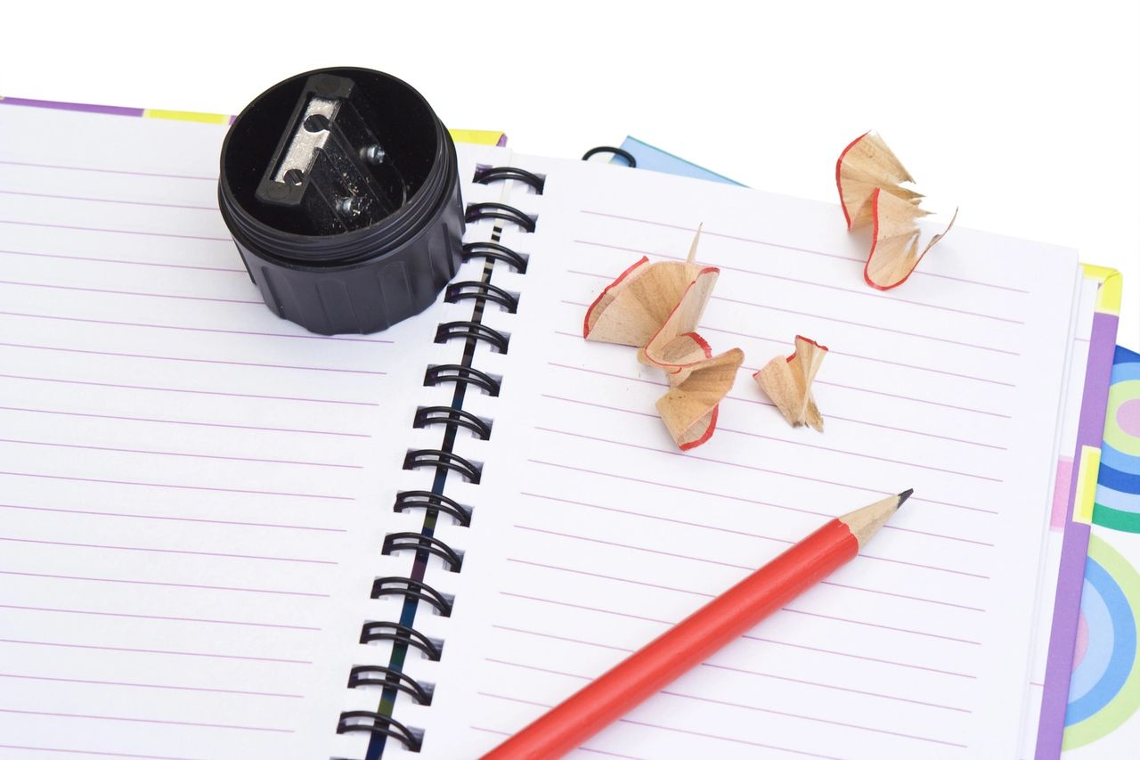 A pencil was just sharpened as the shreds and pencil sharpener sit on top of the notebook.