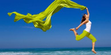 Joyous side effects running on the beach in green pants. a white tank top and a flowing scarf