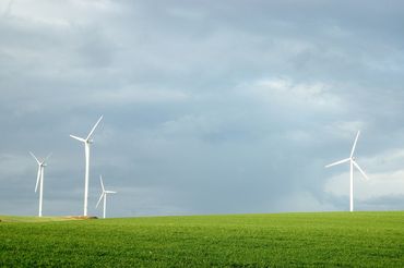 Wind turbines stand tall on a green field under a cloudy sky.