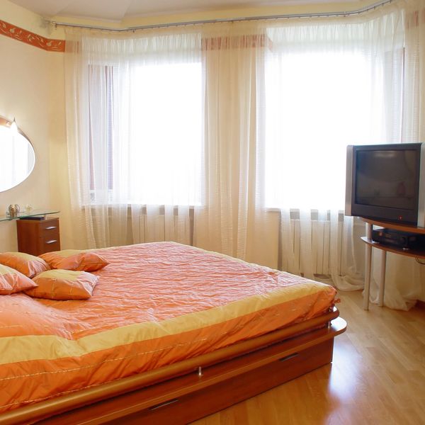 Bright bedroom with a wooden bed and TV near large windows.