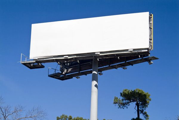Empty white billboard against blue sky.