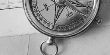 Black and white photo of a compass resting on a map.