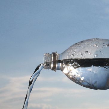 Water pouring from a plastic bottle against the sky.
