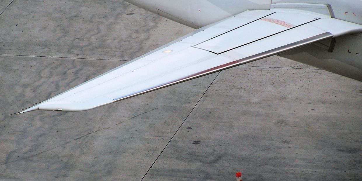 Close-up of an aircraft's white wing against a concrete surface.