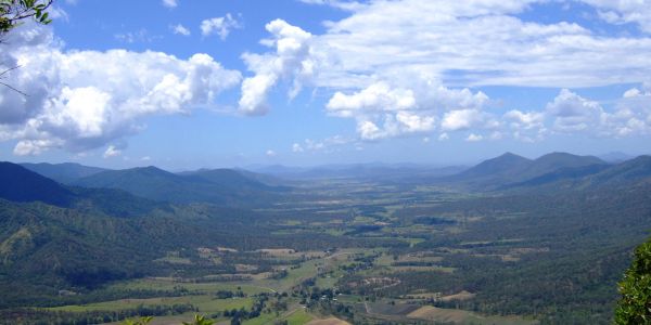 A vast valley surrounded by mountains under a bright blue sky with clouds.