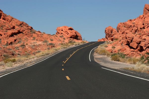 Road winding through red rock desert landscape under clear blue sky.
