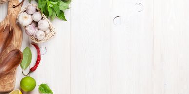 Fresh herbs, garlic, chili, lime, and wooden spoons on a light wooden surface.