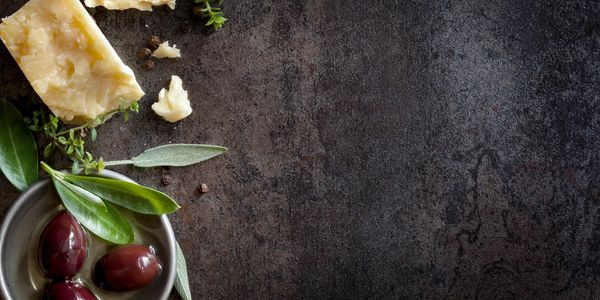 Olives in a bowl next to cheese on a black table.