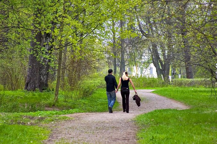 a couple walking hand-in-hand down a paved road with trees and green grass all around them.