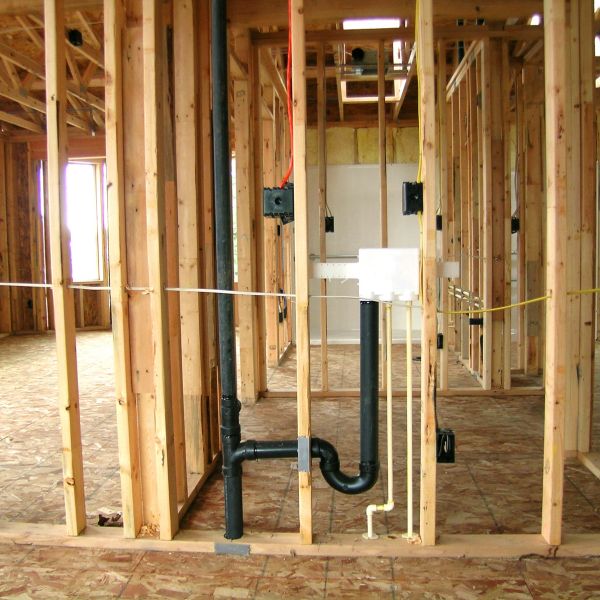 Interior view of a house under construction showing wooden framing and plumbing.