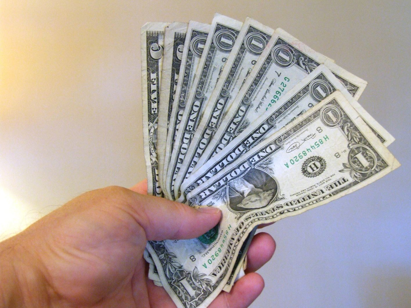 Hand holding several one-dollar bills fanned out.