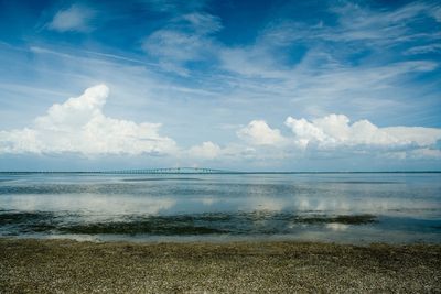 Calm sea with a distant bridge under a partly cloudy blue sky.