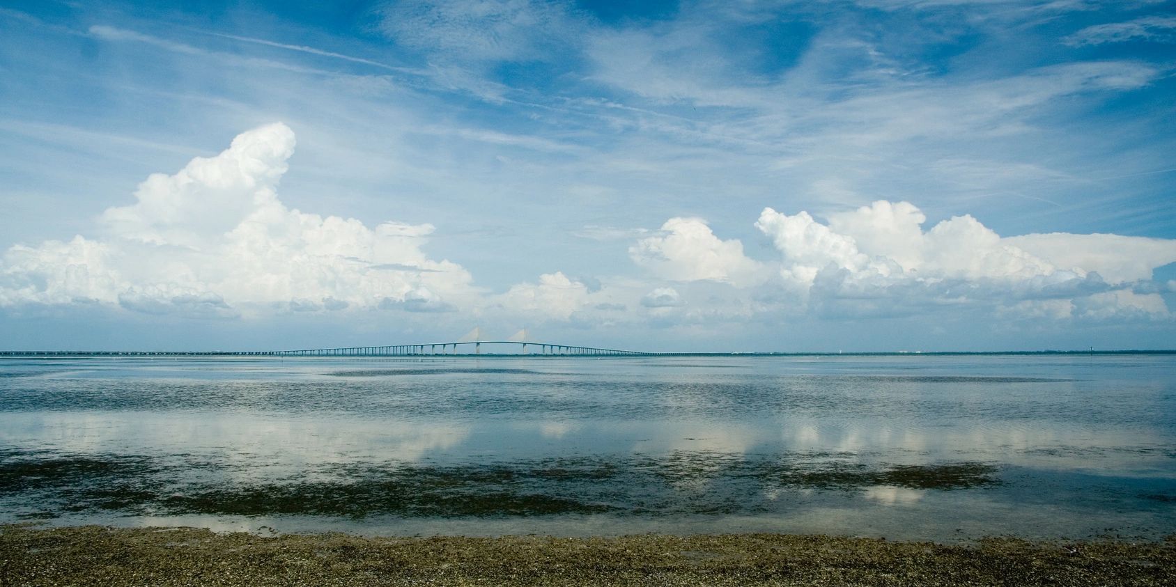A long bridge stretches across calm water under a partly cloudy sky.