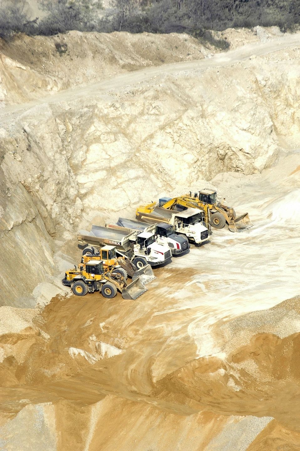 Five heavy construction vehicles lined up in a quarry.