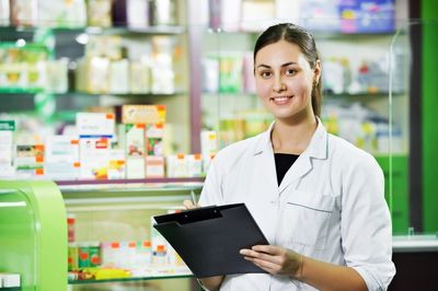 Pharmacist smiling with clipboard in a pharmacy.