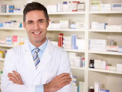 Smiling male pharmacist in white coat standing in a pharmacy.