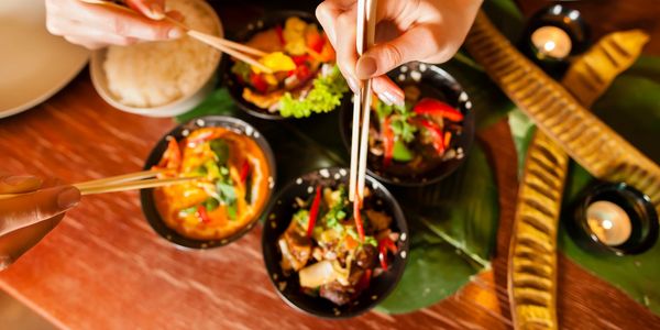People enjoying a vibrant Asian meal using chopsticks.