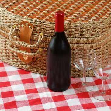 Wine bottle and two glasses on a red and white checkered picnic blanket.