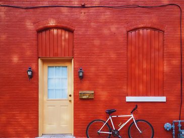 Bicycle parked against a bright red brick wall with a beige door.