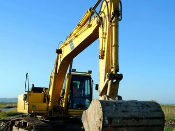 Yellow excavator parked on a construction site under a clear blue sky.