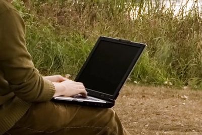 Man on his laptop near a lake outside