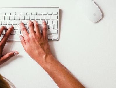 Hands typing on a white keyboard with a white mouse nearby.