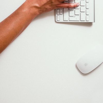 Person's hand typing on a white keyboard next to a white Apple mouse on a clean desk.