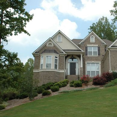 Large suburban house with brick and siding exterior on a grassy hill.