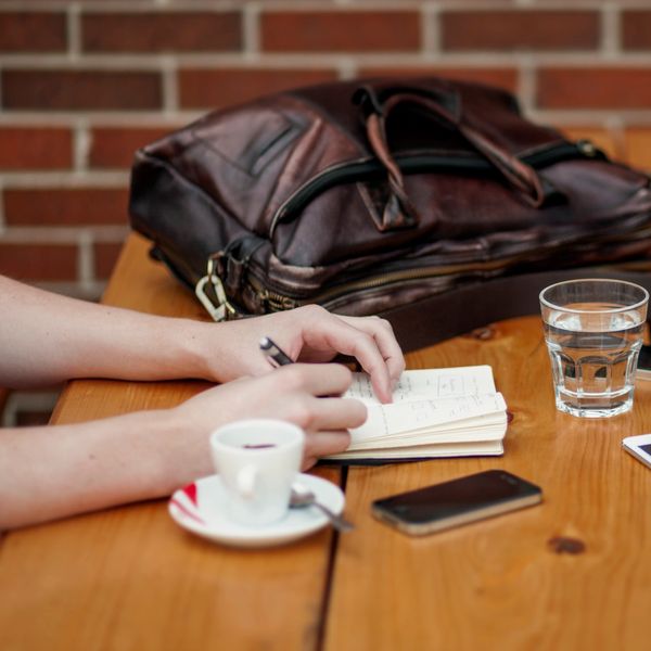 Two people at a wooden table with a notebook, tablet, and coffee.