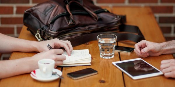 Two people working at a table with notebook, tablet, and coffee.