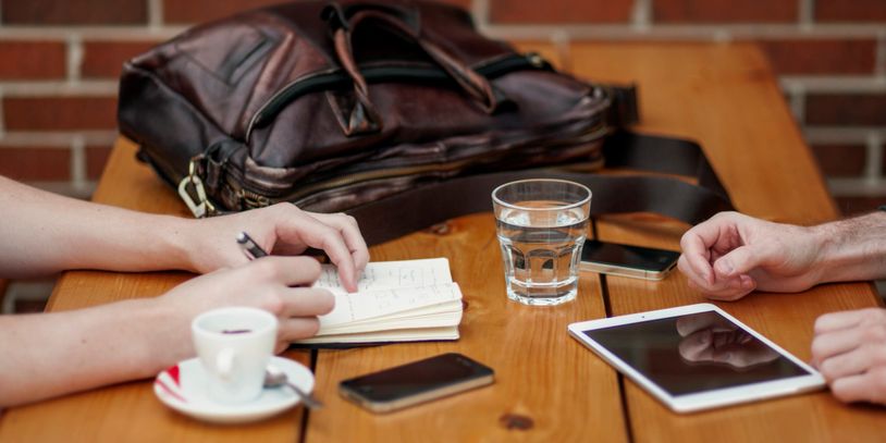 Table with coffee cup, water glass, phone, iPad, notebook