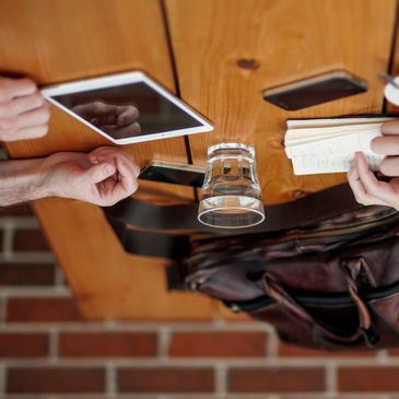 Two people using a tablet and notebook at a wooden table with a glass of water.