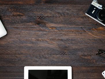 A wooden desk with a tablet, camera, and other gadgets.