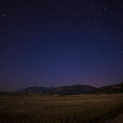 Starry night sky over mountains and open field.