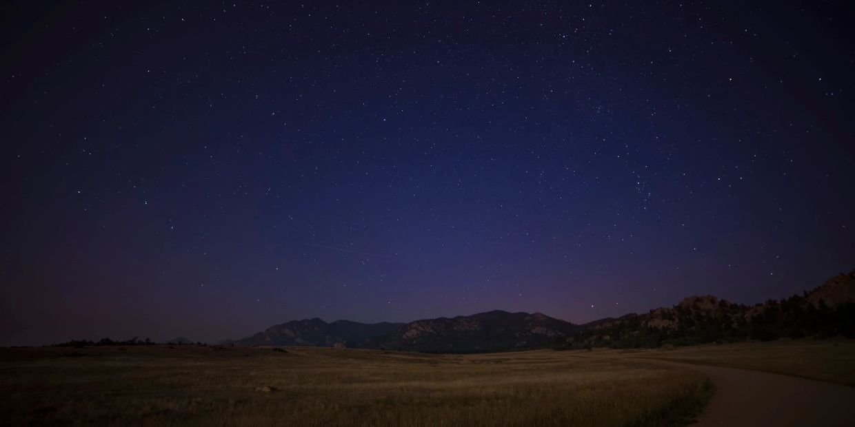 Starry night sky over a mountainous field.